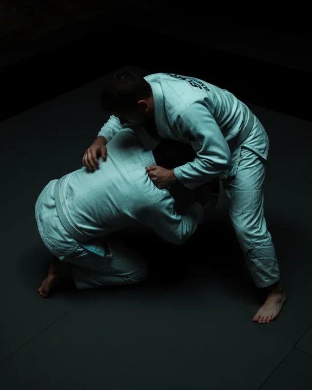 Two practitioners training jiu-jitsu in gi on the mats
